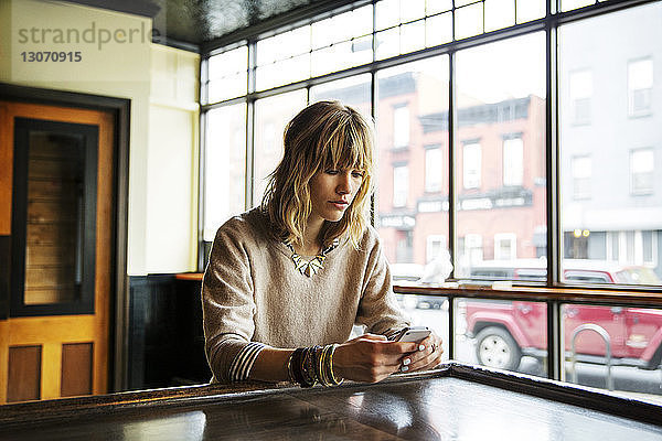 Frau benutzt ein Smartphone  während sie an einem Tisch in einer Bar sitzt