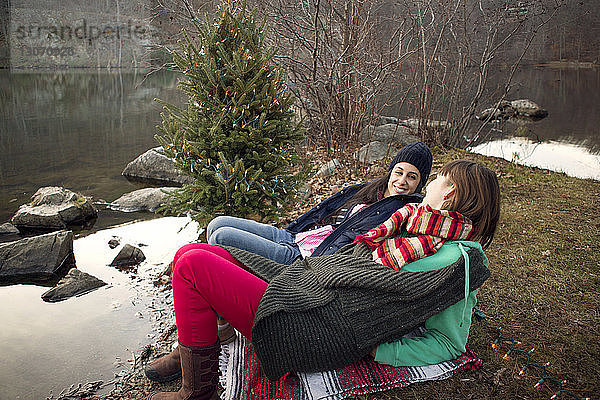 Freunde schauen sich beim Entspannen am Seeufer am Weihnachtsbaum an
