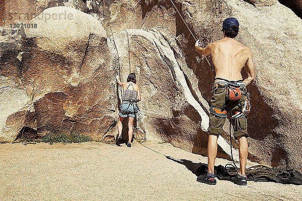 Rückansicht von Freunden  die sich an einem sonnigen Tag auf das Klettern am Fels vorbereiten