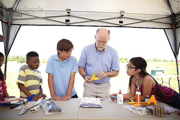 Kinder schauen einem älteren Mann beim Modellbau einer Rakete im Park zu