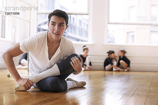 Lächelnder Balletttänzer übt  während er im Studio auf dem Parkettboden sitzt