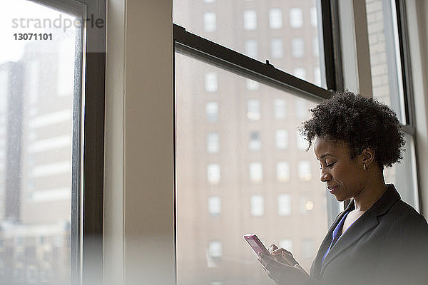Geschäftsfrau benutzt Telefon  während sie im Büro am Fenster steht
