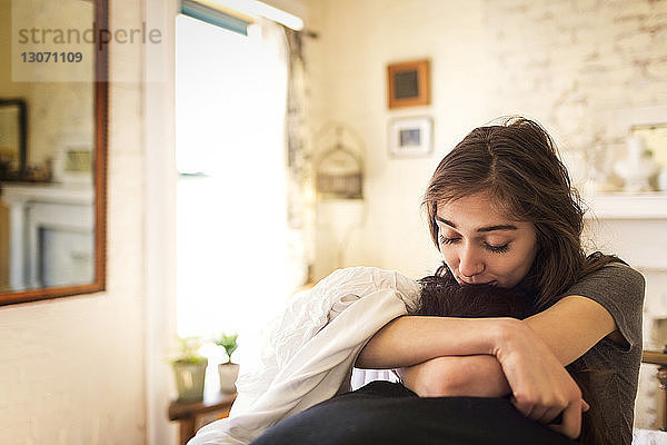 Frau  die den Kopf eines Mannes küsst  während sie zu Hause auf dem Bett sitzt