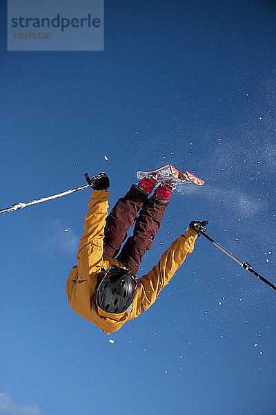 Niedrigwinkelansicht eines Mannes  der beim Skifahren vor klarem  blauem Himmel einen Stunt macht