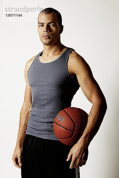 Porträt eines Mannes  der einen Basketball hält  während er vor weißem Hintergrund steht