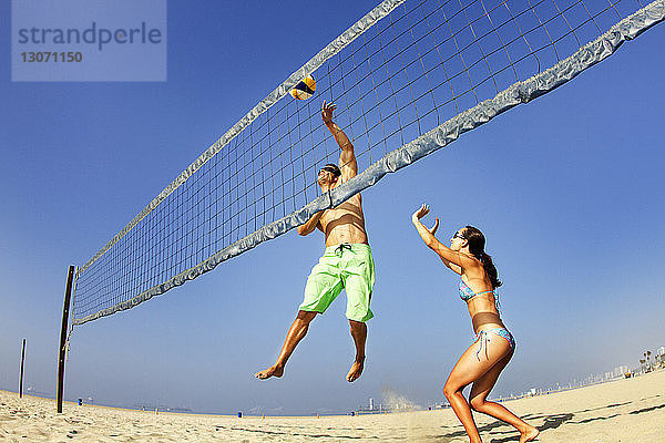 Spielerisches Paar spielt Beach-Volleyball gegen klaren Himmel