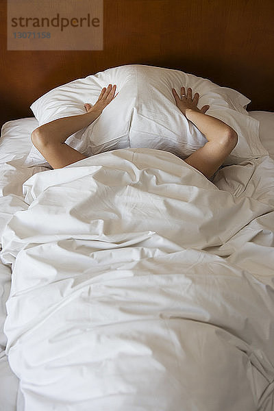 Hochwinkelansicht einer Frau  die ihr Gesicht mit einem Kissen auf dem Bett bedeckt