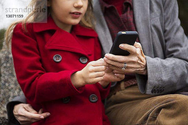 Ein Teil der Familie benutzt ein Mobiltelefon  während er im Park auf einer Bank sitzt