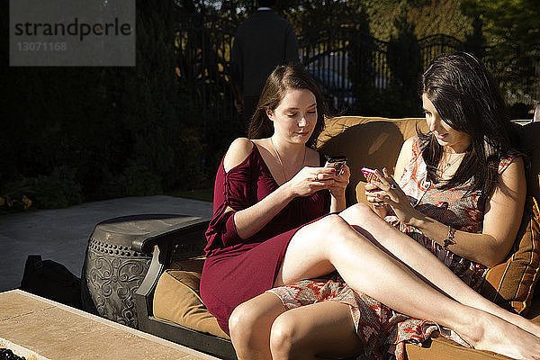Frauen  die ein Mobiltelefon benutzen  während sie auf dem Sofa sitzen