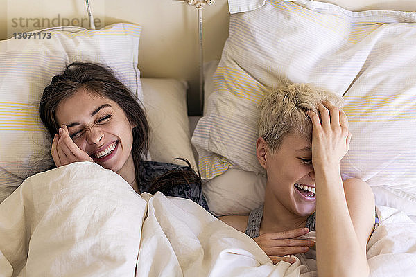 Draufsicht auf glückliche Freunde  die zu Hause auf dem Bett liegen