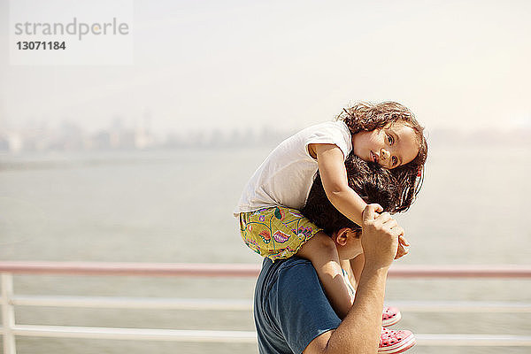 Seitenansicht eines Vaters  der seine Tochter auf der Schulter gegen den Himmel trägt