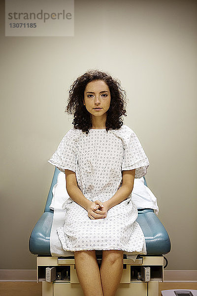 Porträt einer Frau mit gefalteten Händen  die im Krankenhaus auf einem Bett sitzt