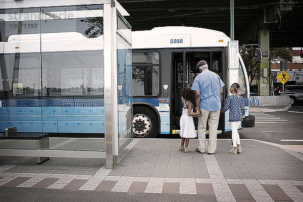 Rückansicht von Großvater und Enkelkindern  die in der Stadt auf den Bus zugehen