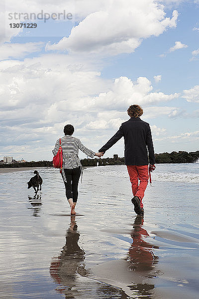Rückansicht eines Paares  das am Strand am Ufer gegen den Himmel läuft