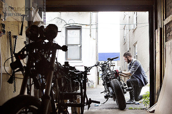 Seitenansicht eines Mannes  der ein Motorrad vor der Werkstatt repariert