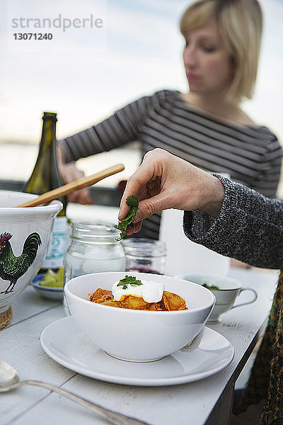 Frau garniert Essen  während sie mit einem Freund am Tisch in der Veranda sitzt