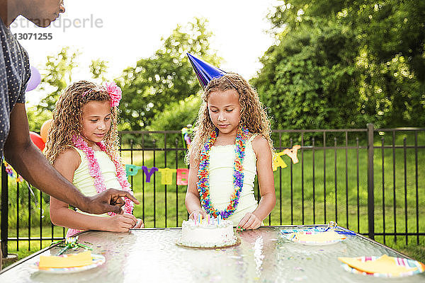 Vater steht bei Mädchen mit Geburtstagskuchen am Tisch im Hinterhof