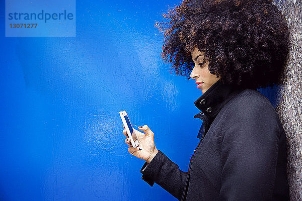 Seitenansicht einer Frau  die telefoniert  während sie an der blauen Wand steht