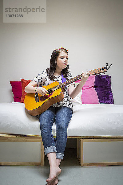 Mädchen spielt Gitarre  während sie zu Hause auf dem Sofa sitzt