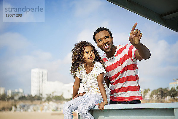 Mann zeigt auf ihn  während er sich mit seiner Tochter am Strand am Pier vergnügt