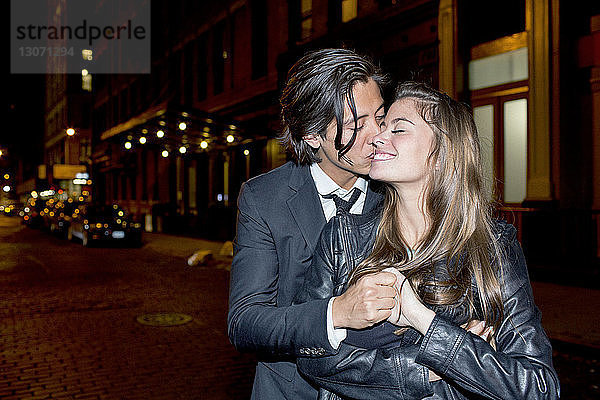 Romantischer Mann küsst seine Freundin  während er nachts auf der Straße der Stadt steht