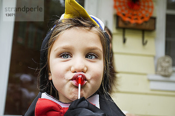 Mädchen in Halloween-Kostüm isst Lolli  während sie gegen das Haus steht