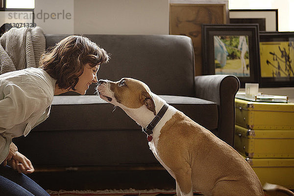 Frau reibt sich zu Hause mit Hund die Nase