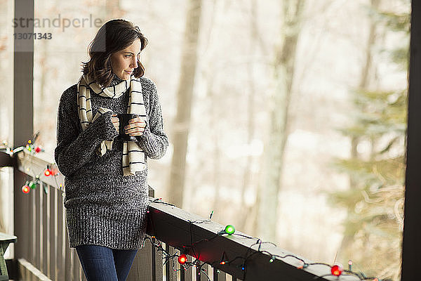 Nachdenkliche Frau mit Kaffeetasse schaut weg  während sie am Geländer steht