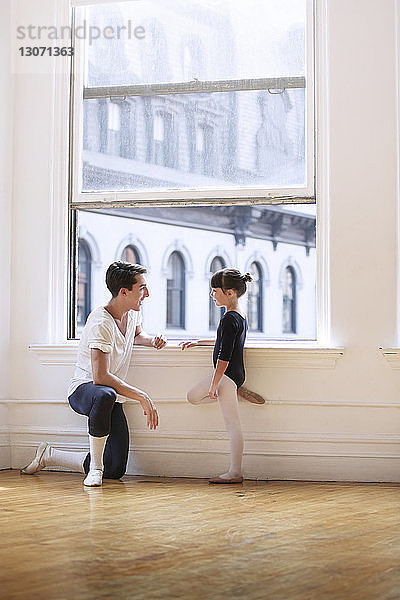 Seitenansicht eines männlichen Ballettlehrers im Gespräch mit einer Ballerina am Fenster im Studio