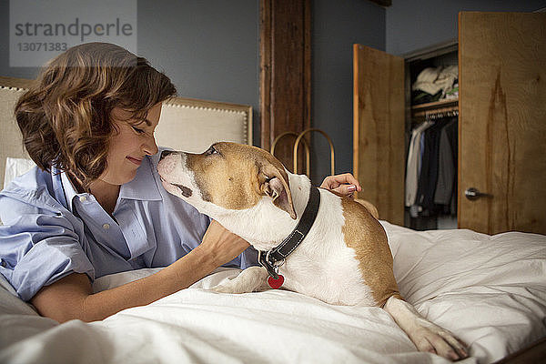 Lächelnde Frau spielt zu Hause mit Hund auf dem Bett