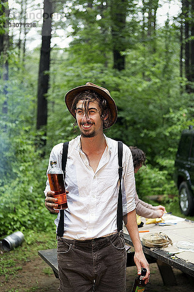 Mann hält Bärenflaschen und schaut weg  während er im Wald steht