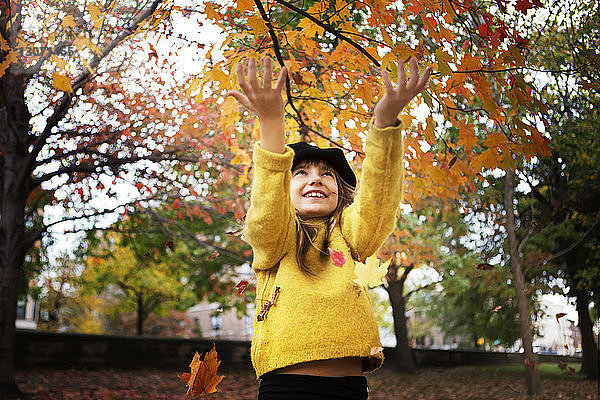 Fröhliches Mädchen spielt im Herbst im Park mit Ahornblättern