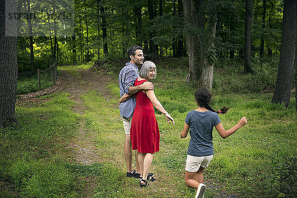 Mädchen rennt auf Großmutter und Vater zu  auf einem Pfad zwischen Bäumen im Wald