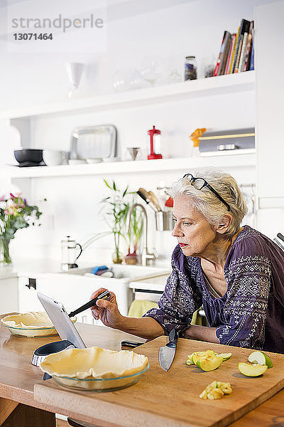 Frau benutzt Tablet-Computer beim Apfelkuchenbacken in der Küche