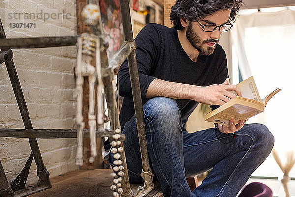 Mann liest Buch  während er zu Hause auf der Treppe sitzt