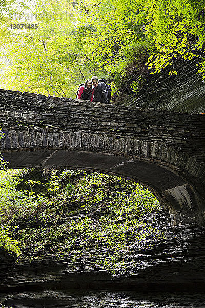 Ehepaar schaut nach unten  während es auf einer Brücke im Wald steht