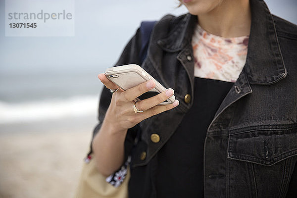 Mitschnitt einer Frau  die ein Smartphone benutzt  während sie am Strand steht