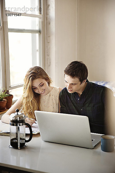 Lächelndes Paar schaut nach unten  während es zu Hause mit einem Laptop-Computer sitzt