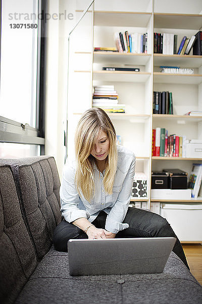Frau benutzt Laptop  während sie zu Hause sitzt