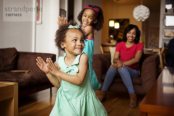 Mutter schaut auf glückliche Töchter  die im Wohnzimmer tanzen