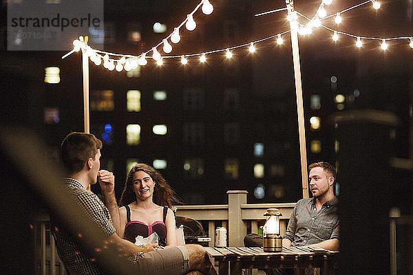Freunde unterhalten sich  während sie abends auf der Terrasse des Gebäudes sitzen