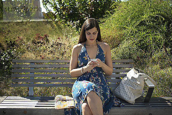 Frau benutzt Smartphone  während sie im Park auf einer Bank sitzt