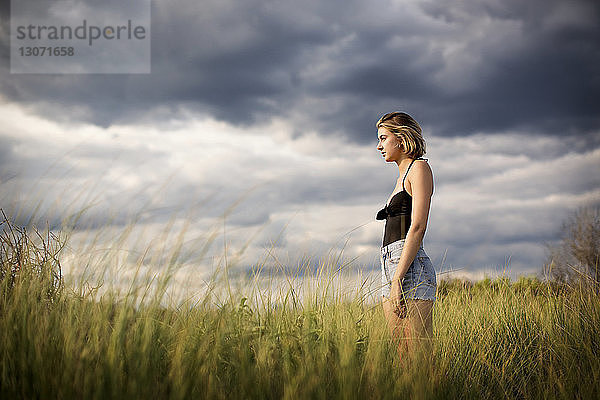 Seitenansicht einer Frau  die auf einem Grasfeld vor bewölktem Himmel steht