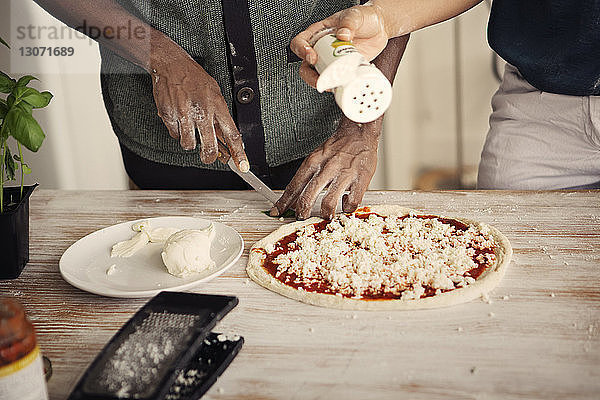 Mittelteil eines Paares  das Pizza zubereitet  während es am Küchentisch steht