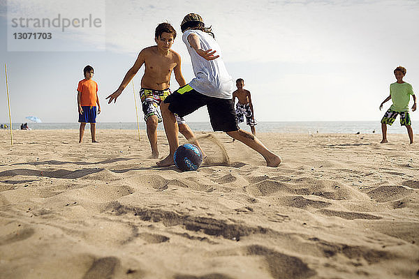 Freunde spielen Fussball am Strand gegen das Meer