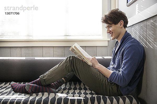 Seitenansicht eines Mannes  der lächelt  während er zu Hause ein Buch liest