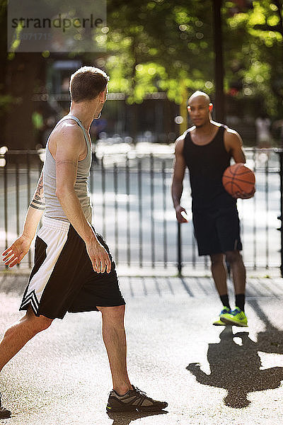 Freunde üben an einem sonnigen Tag Basketball auf dem Platz