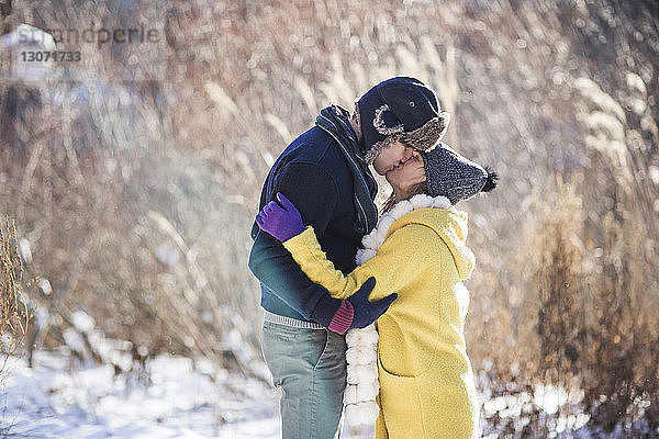 Seitenansicht eines Paares  das sich küsst  während es auf einem schneebedeckten Feld steht
