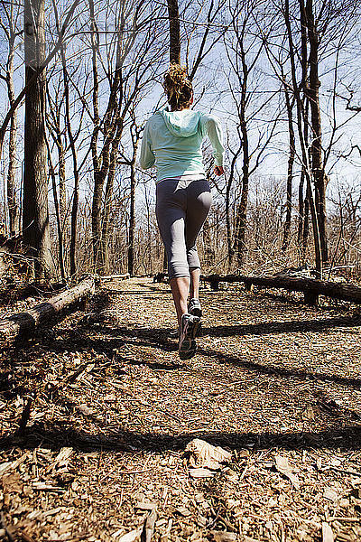 Rückansicht einer Frau  die auf einem Feldweg inmitten kahler Bäume joggt