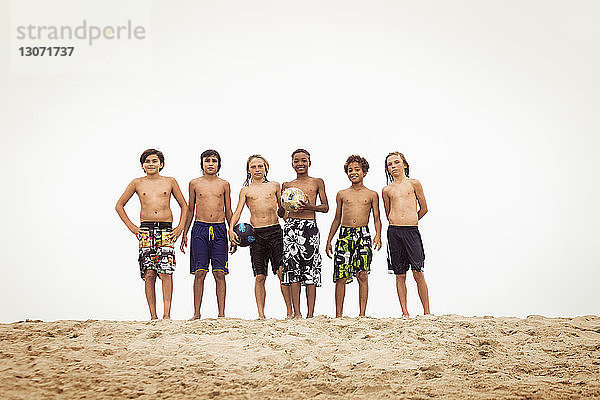 Porträt von Jungen  die auf Sand vor klarem Himmel stehen